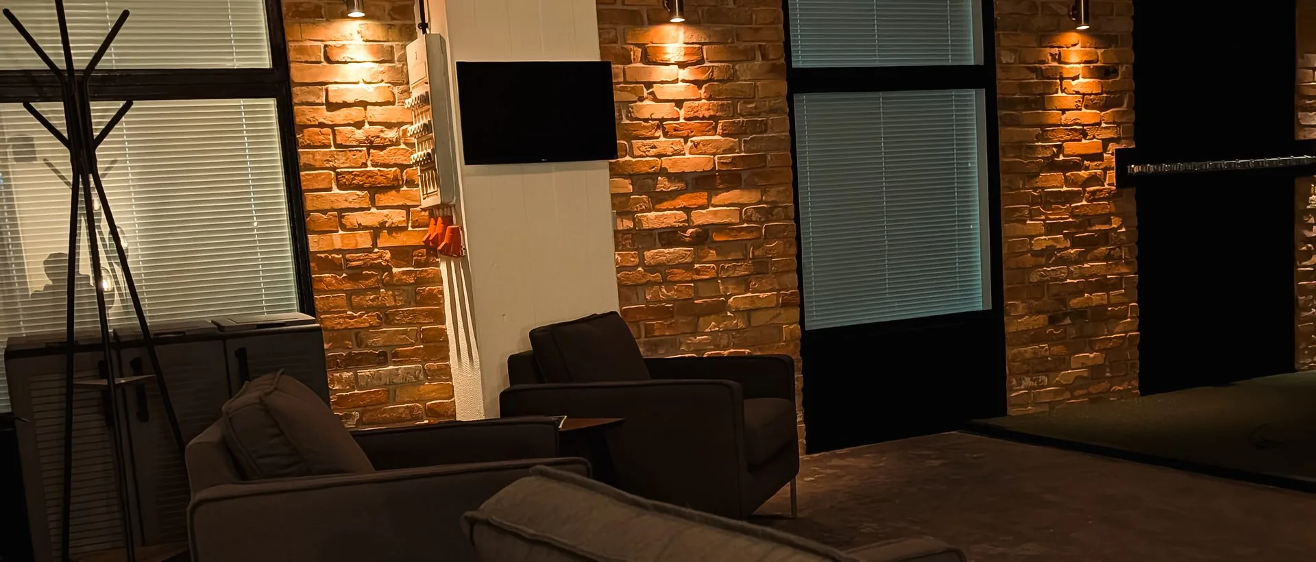 Lounge mit Sesseln vor beleuchteter Backsteinwand bei Birdies Indoor Golf