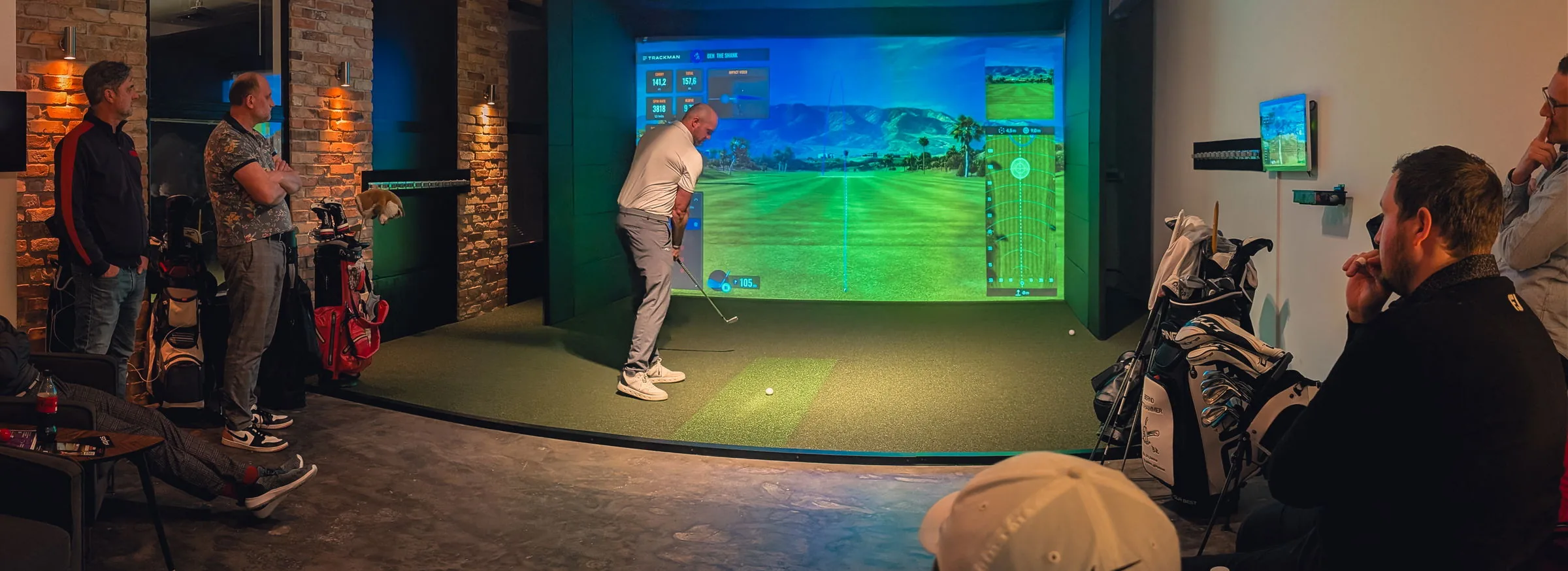 Firmengruppe bei Birdies Indoor Golf N&uuml;rnberg: ein Spieler am Abschlag, die Kollegen verfolgen den Schlag von der Lounge aus