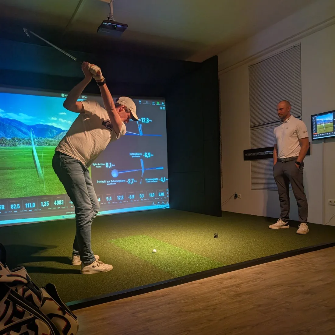 Golf-Training bei Birdies – ein Spieler im Top of Swing am Trackman-Simulator, daneben beobachtet ein PGA-Pro den Schwung